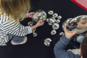 Picture of children seeing their reflection looking into mirrored pebbles