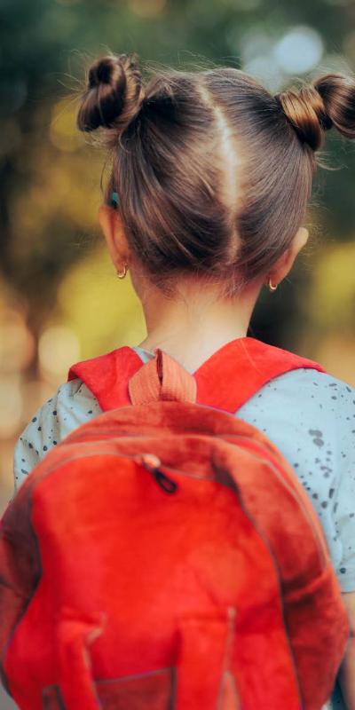 A young girl from behind with bunches in her hair and carrying a red school bag.