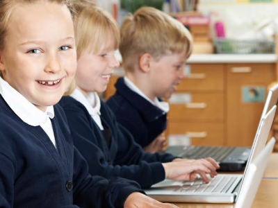 three pupils in school uniform working on laptops.