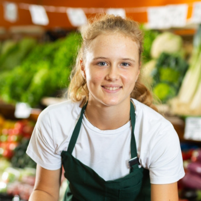 A school age girl working in a grocers shop.