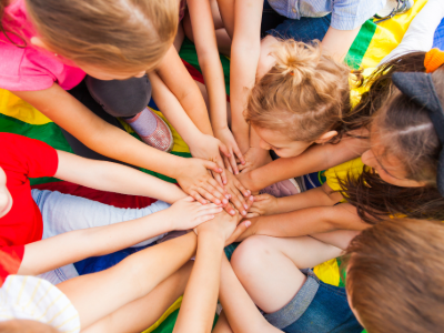 A group of children with arms outstretched and hands touching in the middle of a circle.