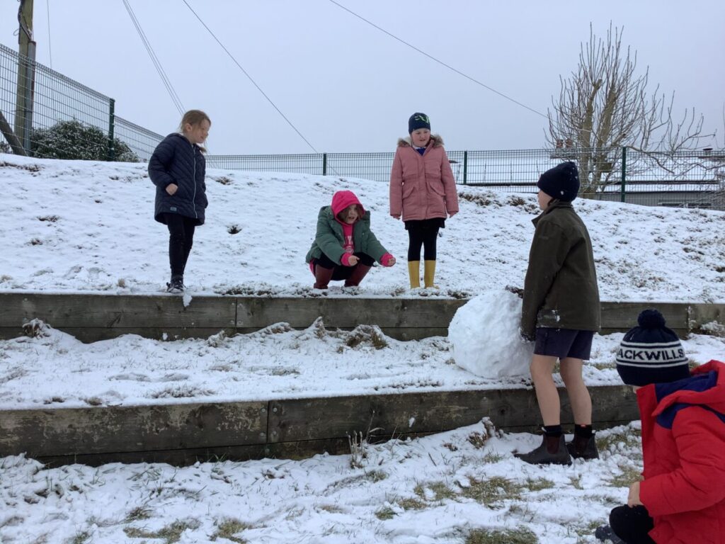 The children enjoying the snow making a giant snowball for their snowman