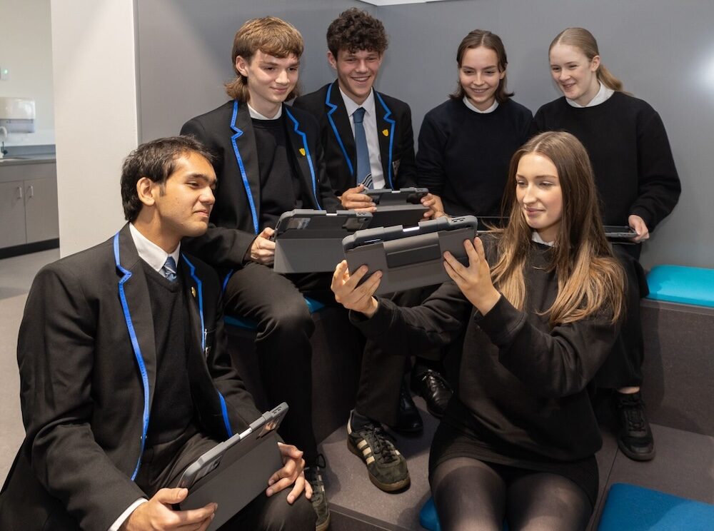 Pupils sitting with individual iPads and one pupil showing the other pupils their iPad.