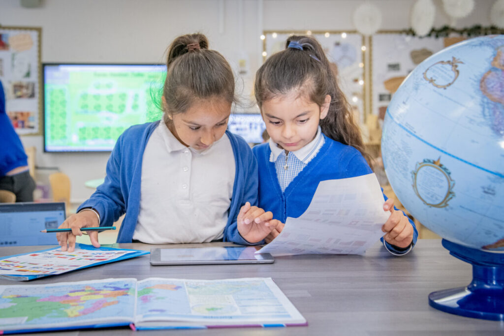 two children looking for information on an ipad and holding a sheet of paper