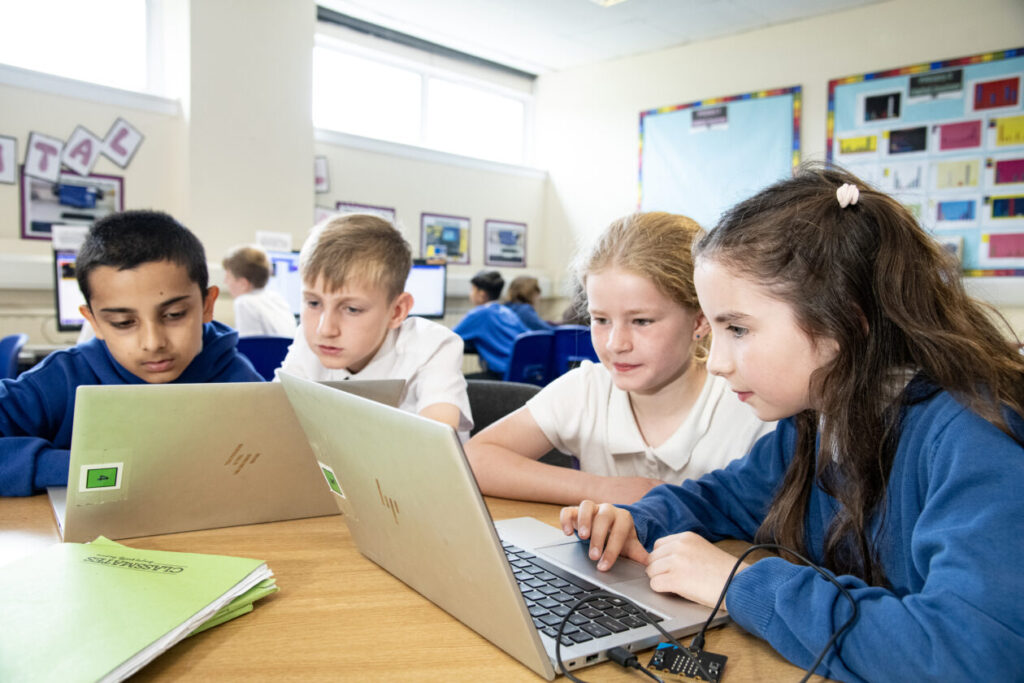four children using laptops in a classroom