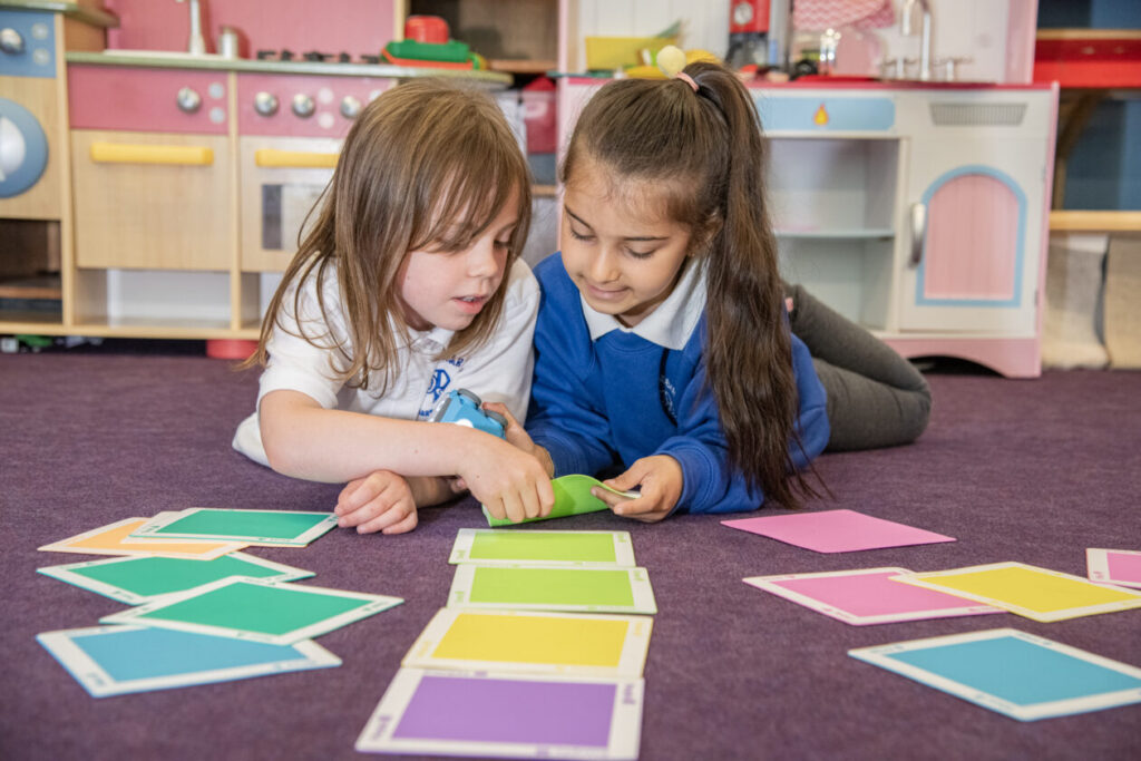 two children guiding a robot along the floor with coloured tiles