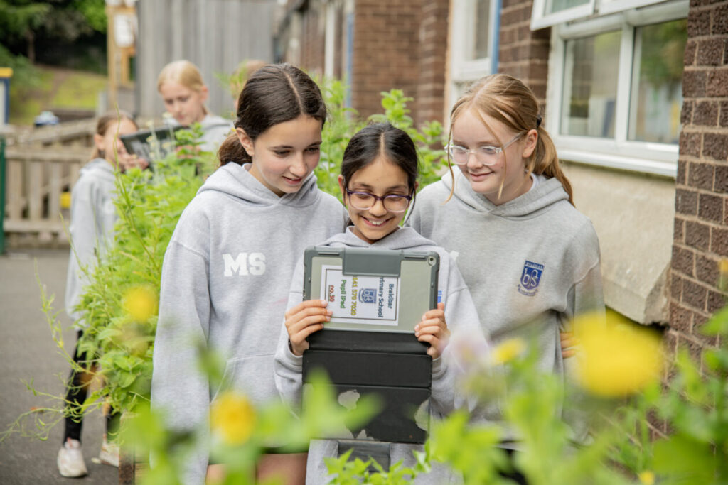 three children using an ipad outdoors to take a picture of flowers