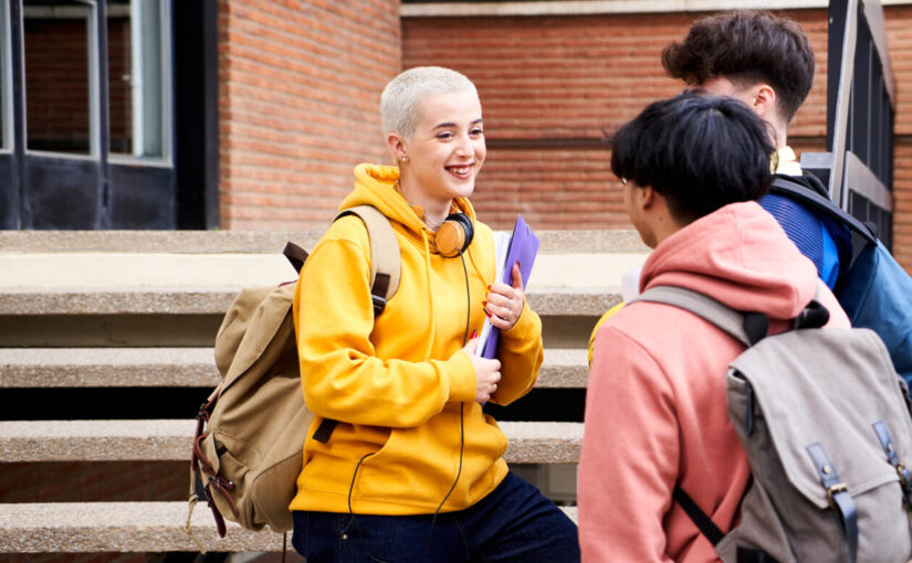 A group of three older teenagers stand outside their learning setting. They are talking and smiling.