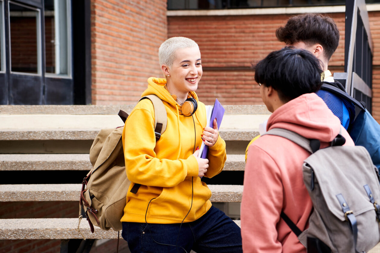 A group of three older teenagers stand outside their learning setting. They are talking and smiling.