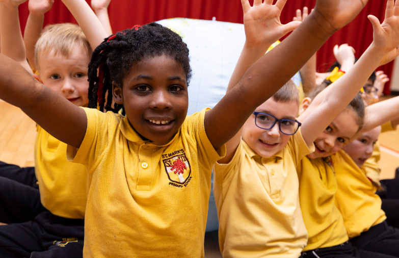 A photo of children smiling and holding their hands in the air. 