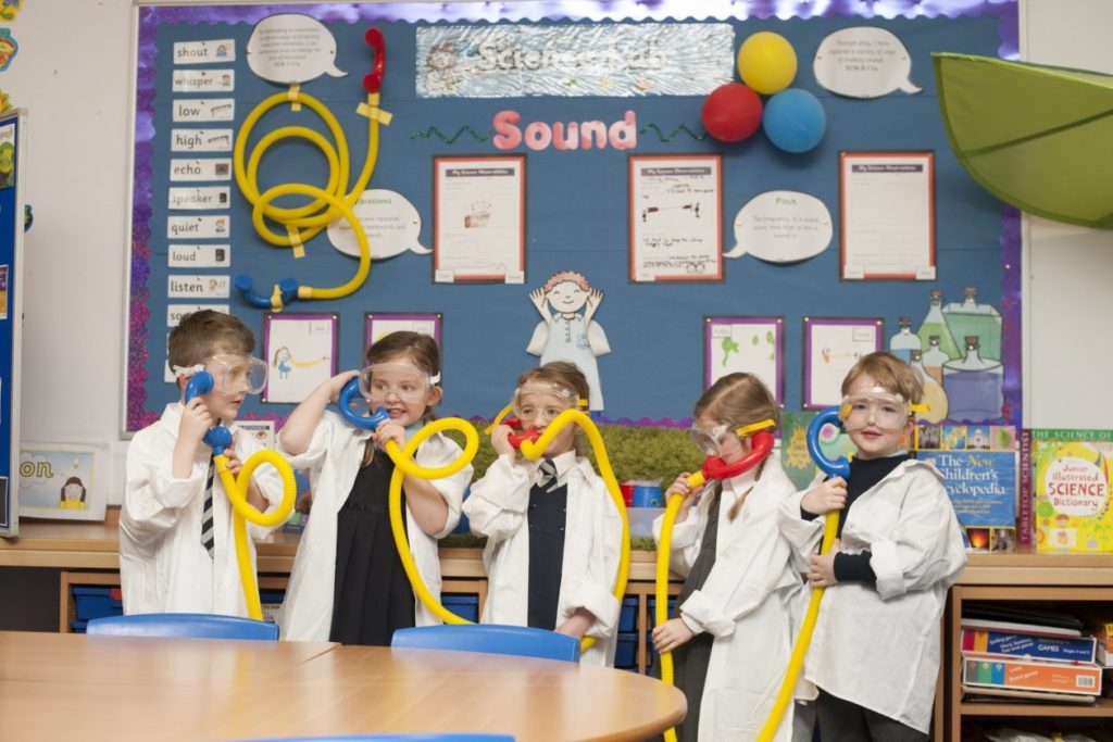 young learners using plastic tubes for pretend telephones