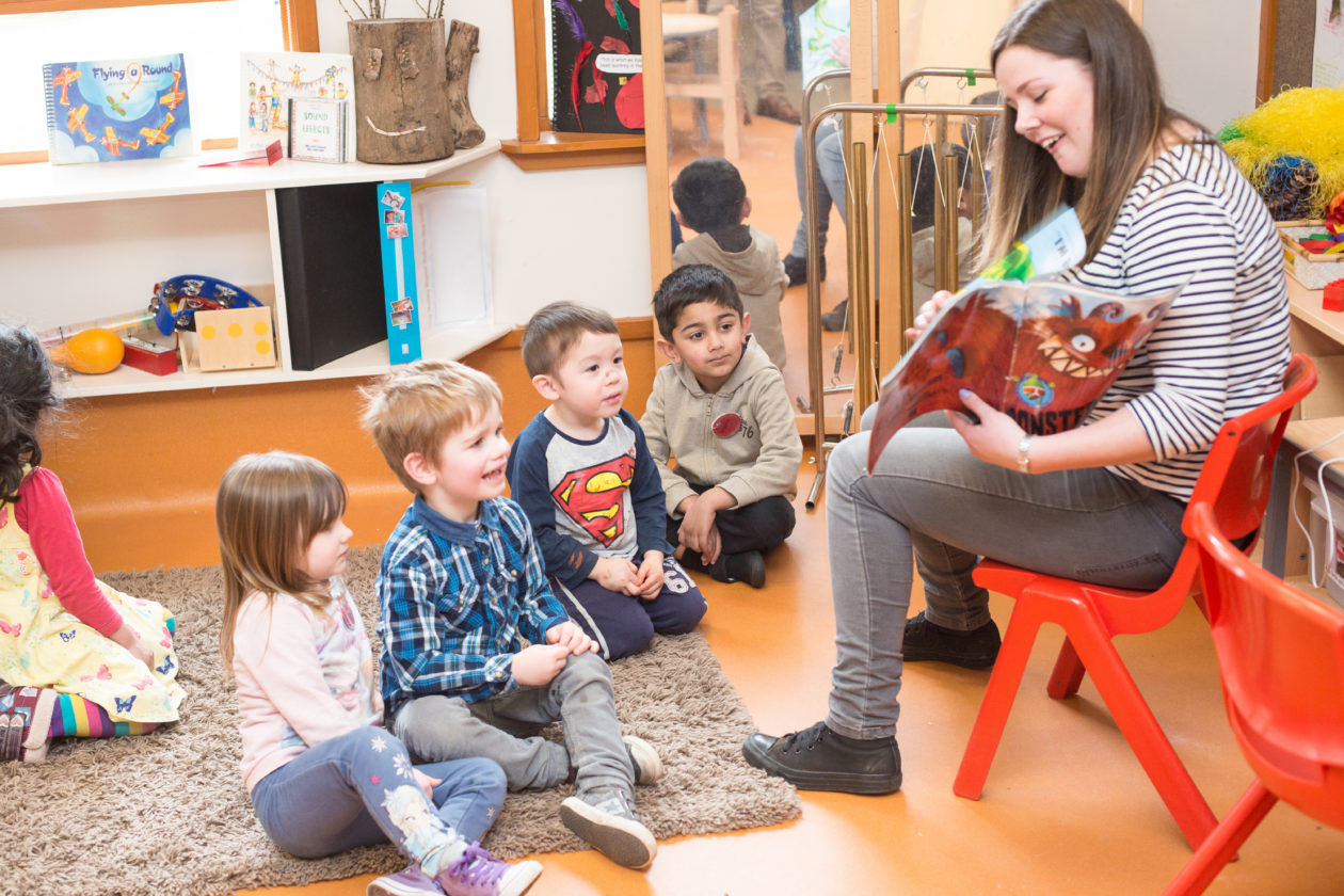 This image shows a practitioner and children engaged in reading a book together. 