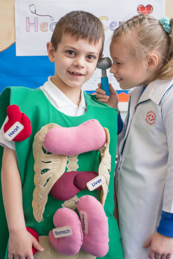 This image shows two children playing, one is taking the role of a medical professional, one is taking the role of a patient. 