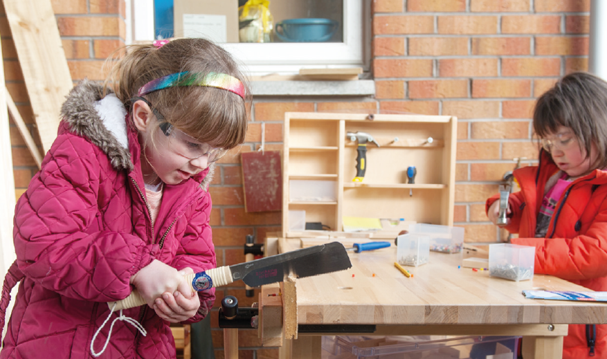 2 early years girls at a workbench using tools for woodwork