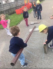 a group of early years children with hard hats building something with tubing and small slabs of concrete