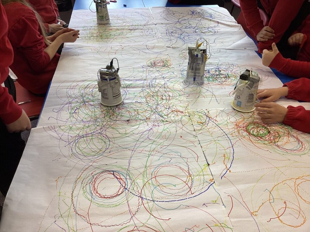 A table with paper and scribble bots drawing over in in colour circles, spirals  and random shapes.