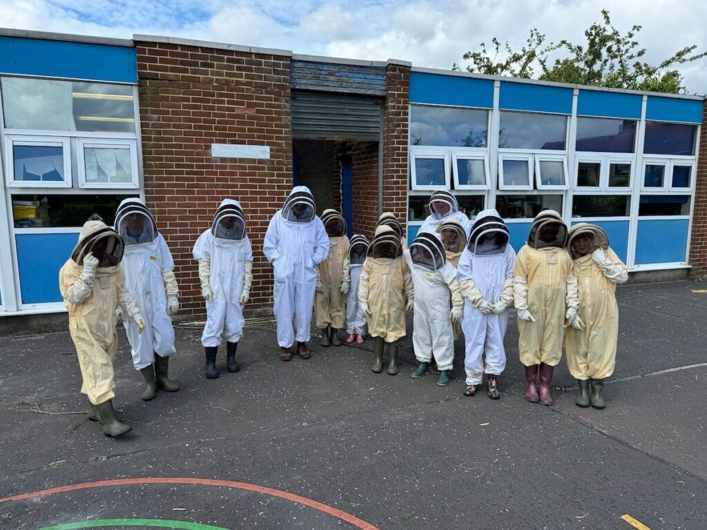 A group of children in beekeeping suits stand outside their school.